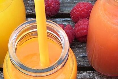Five bottles of colourful smoothies surrounded by fruit, part of a smoothie diet