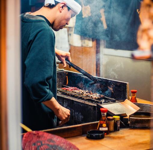 Man cooking meat on skewers: traditional Japanese street food