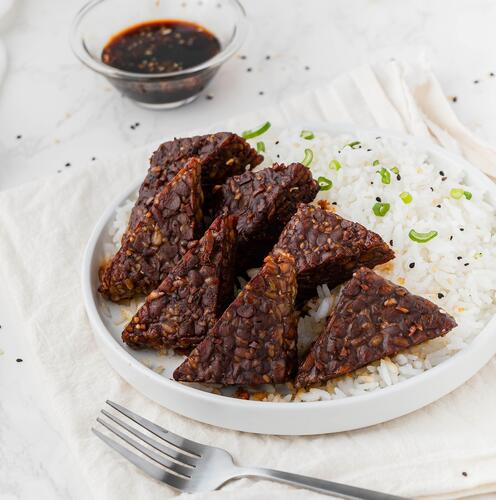 Wooden skewers of cooked tempeh, an example of a vegetarian protein source, with a bowl of orange dip