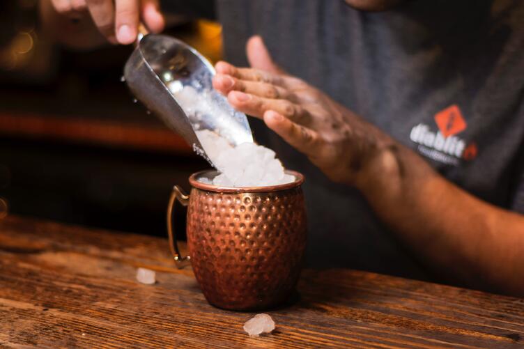 Préparation d’un cocktail Moscow Mule sur un lit de glace pillée, dans une tasse de cuivre