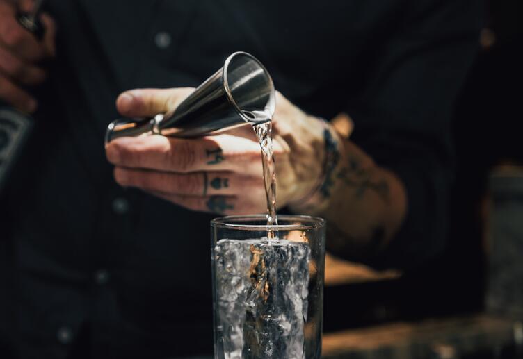 Un barman versant du liquide dans un verre, avec un doseur