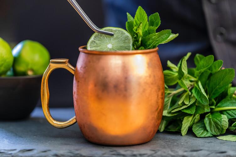 Une pincette déposant une rondelle de citron sur une tasse de Moscow Mule
